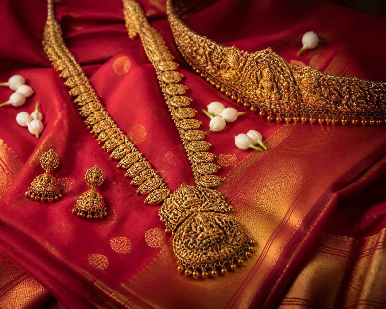 Temple gold jewellery laid across a red kanjeevaram silk saree